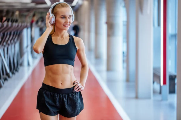 Deporte y música. mujer mantenga los auriculares mientras hace ejercicio en el gimnasio — Foto de Stock