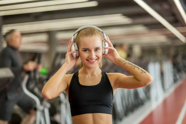 Deporte y música. mujer mantenga los auriculares mientras hace ejercicio en el gimnasio — Foto de Stock