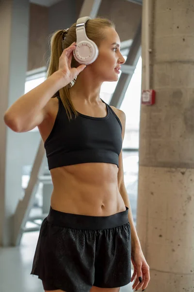 Deporte y música. mujer mantenga los auriculares mientras hace ejercicio en el gimnasio —  Fotos de Stock