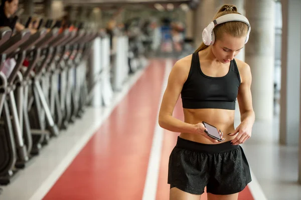 Aktív szőke nő sportruházat használata okostelefon edzőteremben. — Stock Fotó