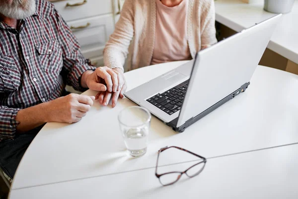 Encantador casal sênior usando laptop sentado à mesa na sala de cozinha. — Fotografia de Stock