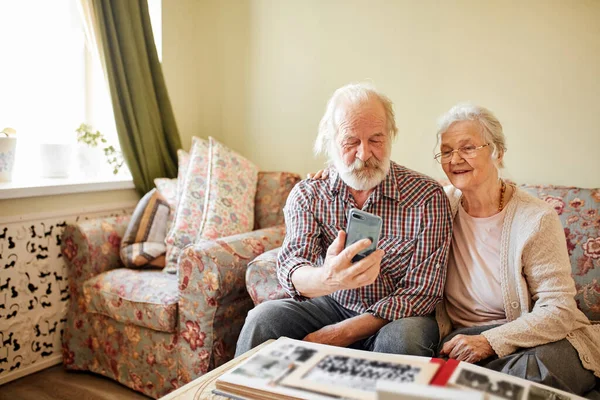 Счастливая пожилая пара со смартфоном делает селфи дома - старость, технологии. — стоковое фото