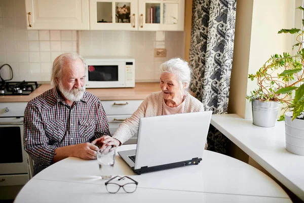 Charmigt par med bärbar dator som sitter vid bordet i köket. — Stockfoto