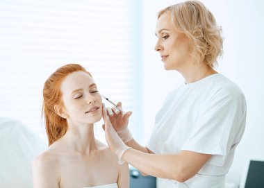 Kafkasyalı kızıl saçlı kadın güzellik yüz enjeksiyonu yaptırıyor. Yaşlanma enjeksiyonu.