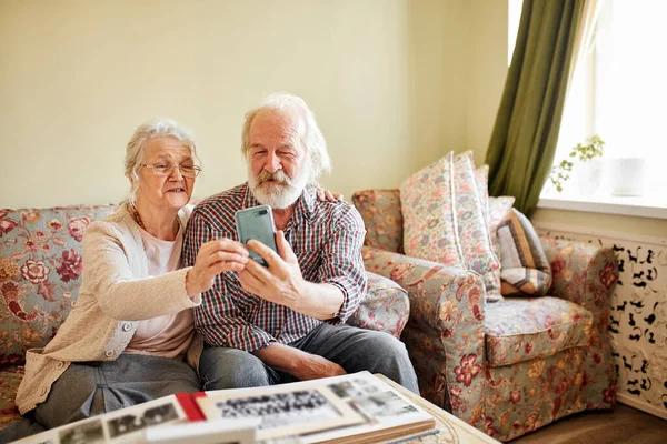 Casal sênior feliz com smartphone levando selfie em casa, velhice, tecnologia. — Fotografia de Stock