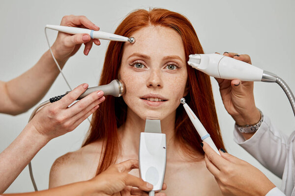 Conceptual image of female emotional face and cosmetologist hands with devices