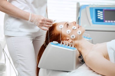 Yüzünde elektrotlar olan genç bir kadın, elektrik uyarısı alıyor..