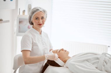 Kozmetik uzmanı pamuklu ped takıyor. Kadın yüzü ameliyata hazırlanıyor..