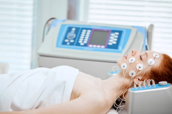 Giovane donna sdraiata con elettrodi, riceve una stimolazione elettrica sulla sua pelle. — Foto Stock