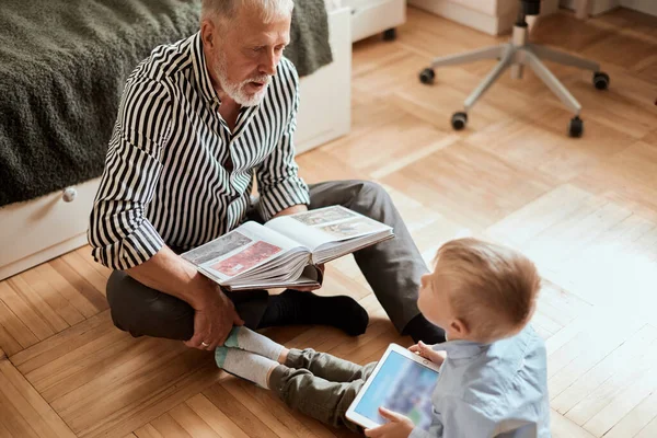 Nonno guarda album fotografico con il suo matrimonio, bambino utilizzando tablet elettronico — Foto Stock