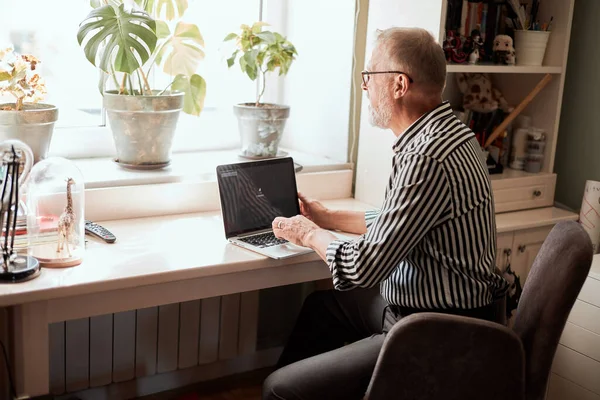 Mature bearded man working from home with laptop. sitting at desk near window — Stock Photo, Image