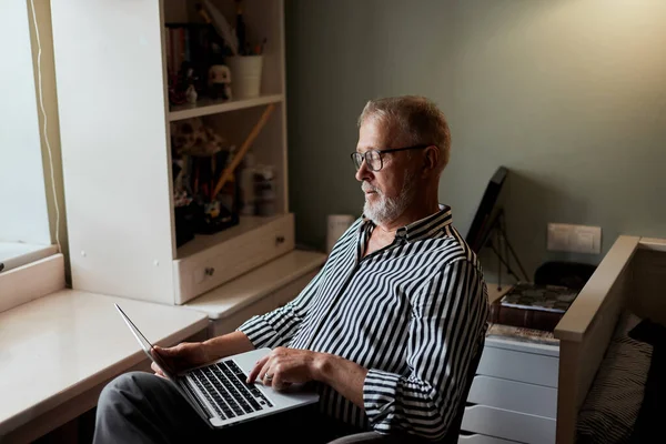 Hombre barbudo maduro que trabaja desde casa con el ordenador portátil. sentado en el escritorio cerca de la ventana — Foto de Stock