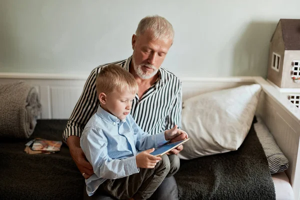 Büyükbaba ve torun koltukta otururken dijital tablet kullanıyorlar. — Stok fotoğraf