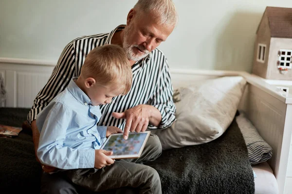 Abuelo y nieto usando tableta digital mientras están sentados en el sofá — Foto de Stock