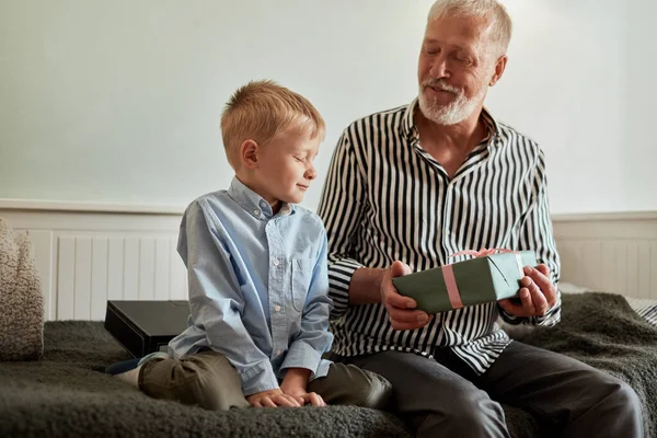 一代。爷爷和孙子带着礼品盒坐在家里的沙发上 — 图库照片