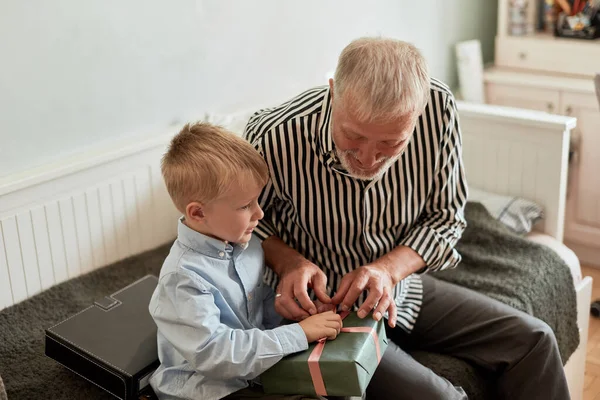 Geração. avô e neto com caixa de presente sentado no sofá em casa — Fotografia de Stock