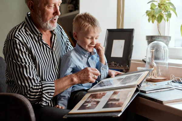 Dědeček a vnuk jsou doma na gauči. Děda a děti se dívají na staré fotky — Stock fotografie