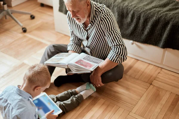 Дедушка смотрит фотоальбом со своей свадьбой, маленький мальчик с помощью электронного планшета — стоковое фото