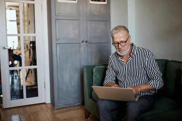 Maturo uomo barbuto che lavora da casa con il computer portatile. seduta alla scrivania vicino alla finestra — Foto Stock