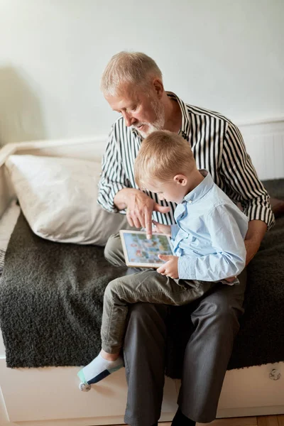 Abuelo y nieto usando tableta digital mientras están sentados en el sofá —  Fotos de Stock