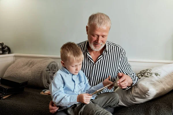 Abuelo y nieto usando tableta digital mientras están sentados en el sofá —  Fotos de Stock