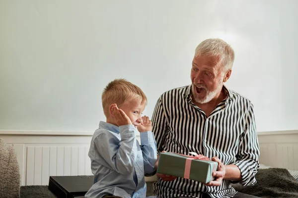 Generation. Großvater und Enkel mit Geschenkbox auf Couch zu Hause — Stockfoto