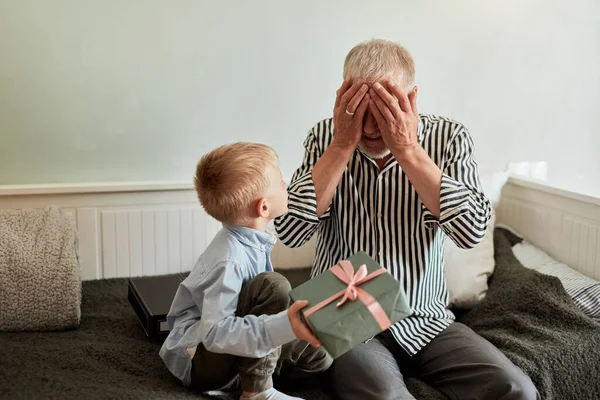 Γενιά. παππούς και εγγονός με κουτί δώρου κάθεται στον καναπέ στο σπίτι — Φωτογραφία Αρχείου
