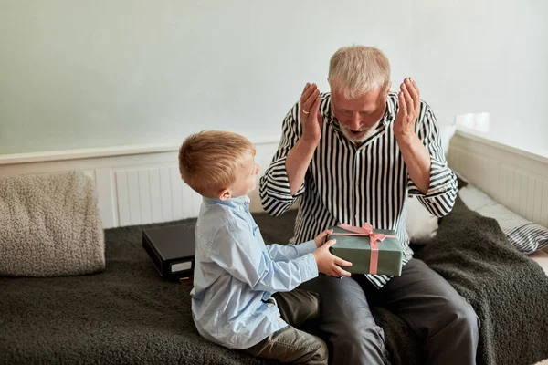 Generation. farfar och sonson med presentförpackning sittandes på soffan hemma — Stockfoto