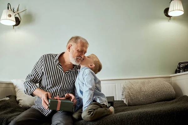 Generation. farfar och sonson med presentförpackning sittandes på soffan hemma — Stockfoto