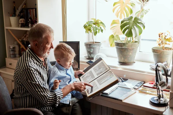 Abuelo y nieto en el sofá en casa. Abuelo y niños viendo fotos viejas — Foto de Stock