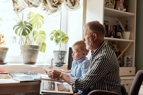 Abuelo y nieto en el sofá en casa. Abuelo y niños viendo fotos viejas —  Fotos de Stock