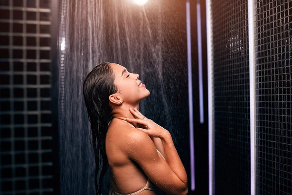 Schöne kaukasische Brünette unter der Dusche in ihrem schwarzen Luxusbadezimmer. — Stockfoto