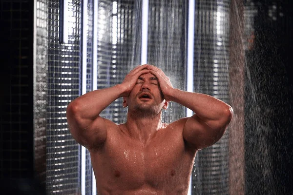 Hombre guapo tomando una ducha, refrescándose después de un día de trabajo caliente . — Foto de Stock