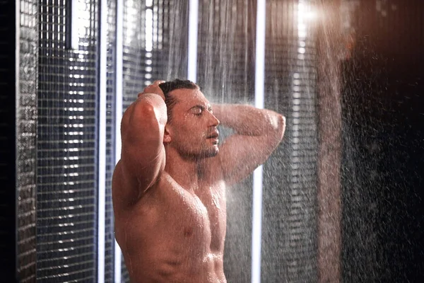 Hombre guapo tomando una ducha, refrescándose después de un día de trabajo caliente . — Foto de Stock