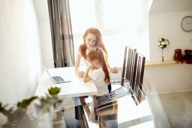 Kızıl saçlı anne ve tatlı kızı dizüstü bilgisayardan çizgi film izliyorlar.