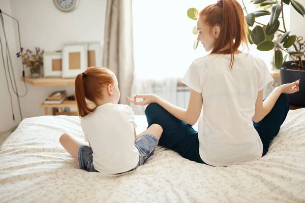 Madre e figlia meditando, esibendosi posa loto mentre seduti sul letto — Foto Stock