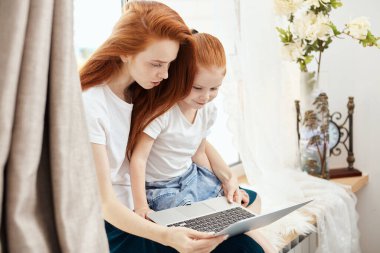 Anne ve kızı evde dizüstü bilgisayar kullanıyorlar.