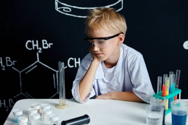Laboratuvar önlüklü küçük bilim adamı siyah gözlükleri ayarlıyor.