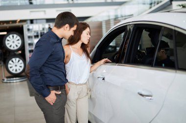 Zarif yaz zamanı kıyafetleri içinde genç bir çift araba galerisinde yeni bir araba seçiyor.