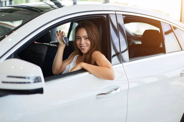 Mujer feliz conductor en coche blanco sostiene las llaves del coche en su nuevo coche en la sala de exposiciones de coches — Foto de Stock