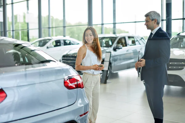 若い女性の顧客は車の販売代理店で助けるために成熟したセールスマネージャーを求めて. — ストック写真