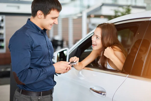 Araba satıcısı araba galerisinde oturan genç bir bayana araba anahtarı veriyor. — Stok fotoğraf