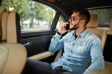 Gülümseyen harika adam arabada otururken telefonda konuşuyor.