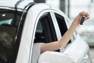 Şen şakrak şoför kadın araba galerisinde otururken gülümsüyor ve yeni anahtar gösteriyor.