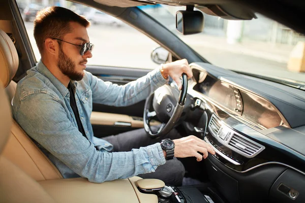 Schöner Mann schaltet Stereoanlage ein, während er Auto fährt — Stockfoto