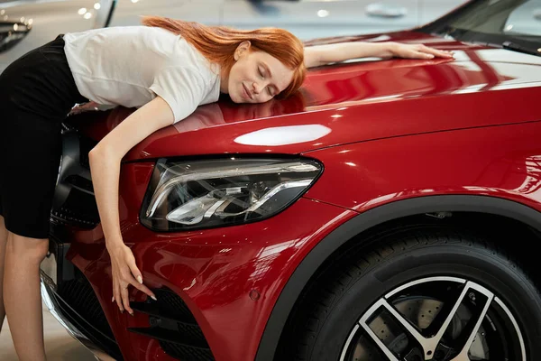 Mulher caucasiana feliz abraçando seu novo carro na concessionária de automóveis — Fotografia de Stock