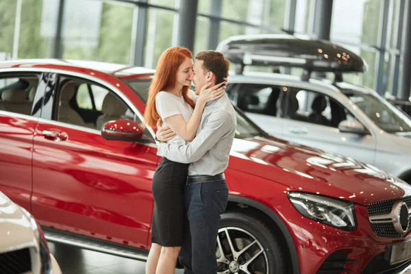 Пара обіймається, купуючи перший новий сімейний автомобіль разом у дилерському центрі . — стокове фото