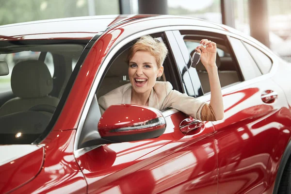 Überglückliche Fahrerin lächelt und zeigt Autoschlüssel, während sie im Autohaus sitzt — Stockfoto