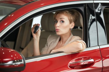 Şen şakrak şoför kadın araba galerisinde otururken gülümsüyor ve yeni anahtar gösteriyor.