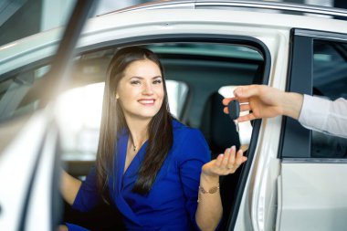 Arabada oturan gülümseyen genç kadın anahtarı alıyor. Kira, satın alma, satma.